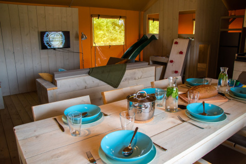 Interior of a glamping tent at De Bosweide, featuring dining table, TV, slide, and kitchen in Noord-Brabant.