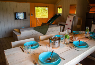 Interior de tienda glamping en De Bosweide con mesa de comedor, TV, tobogán y cocina en Noord-Brabant.