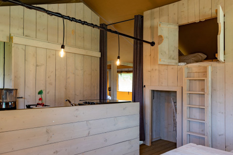 Interior de una tienda glamping con madera clara, cama alta y cocina en Glamping de Bosweide, Noord-Brabant.
