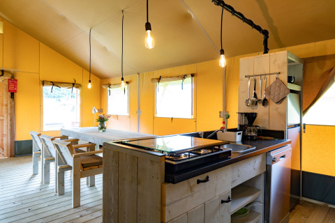Interior view of a luxury glamping lodge tent with dining table and kitchen in Noord-Brabant, Netherlands.