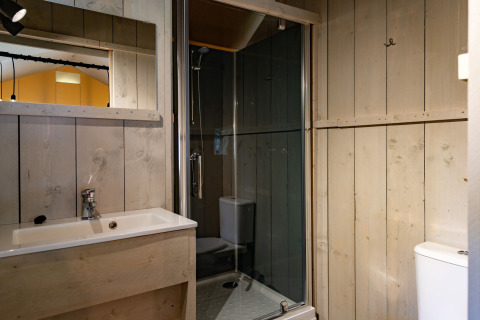 Moderne glamping badkamer met houten wanden, wastafel, spiegel, douche en toilet in Noord-Brabant.