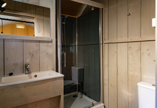 Moderne glamping badkamer met houten wanden, wastafel, spiegel, douche en toilet in Noord-Brabant.