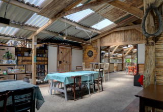 Gezamenlijke binnenruimte bij Glamping de Bosweide met rustieke houten tafels en daglicht in Noord-Brabant.