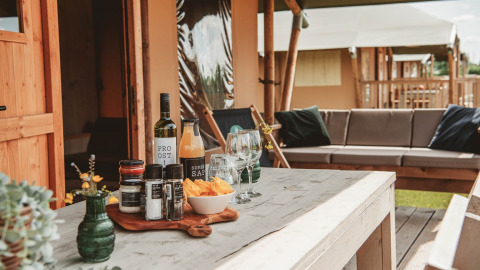 Udendørs glampingbord med snacks, vin og glas foran et luksustelt på Erfgoedpark de Hoop i Nordholland.