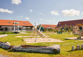Legeplads med træklatrestativ og sand, glampingtelte og bygninger på Erfgoedpark de Hoop i Holland.