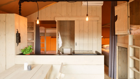 Interior of a luxury glamping tent cabin with kitchenette, bunk beds, and dining table in Noord-Holland.