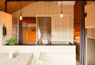 Interieur van een luxe glampingtent met keukenhoek, stapelbedden en eettafel in Noord-Holland.