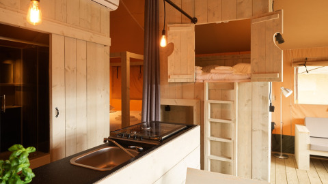 Interior de una tienda glamping en Erfgoedpark de Hoop, Holanda, con muebles de madera y altillo para dormir.