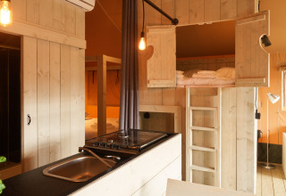 Interior de una tienda glamping en Erfgoedpark de Hoop, Holanda, con muebles de madera y altillo para dormir.