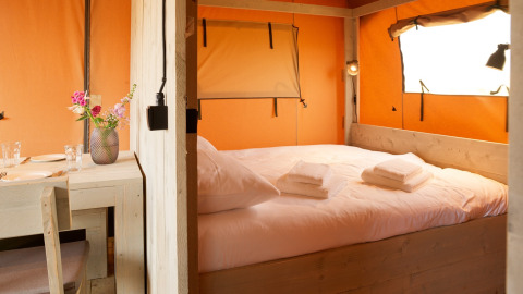 Indretning af et glamping-telt med komfortabel seng og spisebord hos Erfgoedpark de Hoop i Nordholland.