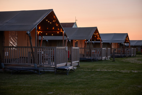 Glamping-Zelte im Erfgoedpark de Hoop in Noord-Holland mit Lichterketten bei Sonnenuntergang.