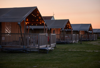 Glamping-telte på Erfgoedpark de Hoop i Noord-Holland, oplyst med lyskæder ved solnedgang.