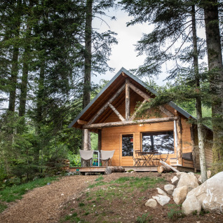 Cabane en bois pour glamping au Village Huttopia Forêt des Vosges, entourée de grands arbres verts