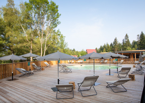 Area piscina con sdraio e ombrelloni al Village Huttopia Forêt des Vosges, immersa nella foresta.