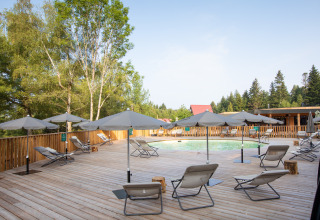 Sunny pool area with loungers and umbrellas at Village Huttopia Forêt des Vosges, surrounded by forest.