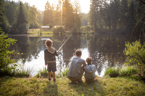 Familie fiske ved en sø omgivet af skov nær Village Huttopia Forêt des Vosges glamping i Vogezen.