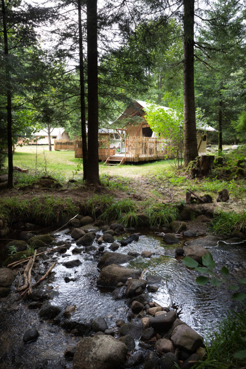 Glamping accommodation at Village Huttopia Forêt des Vosges near a rocky creek in a lush green forest.