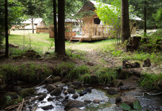 Sistemazione glamping al Village Huttopia Forêt des Vosges vicino a un ruscello in una foresta verde.