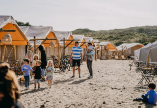 Familier nyder glamping ved Surfana Family Camp Bloemendaal, omgivet af telte og sand i Noord-Holland.