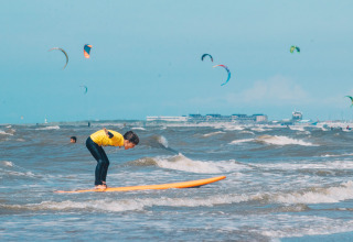 Child surfing at Surfana Family Camp Bloemendaal - Glamping Noord-Holland with kites in the background.