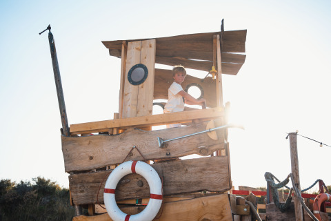 Ein Kind spielt auf einem hölzernen Spielschiff im Sonnenlicht bei Surfana Family Camp Bloemendaal - Glamping Noord-Holland.