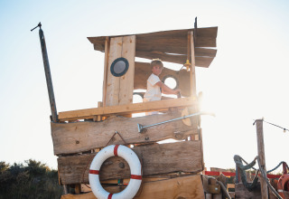 A child plays on a wooden play ship in the sun at Surfana Family Camp Bloemendaal - Glamping Noord-Holland.