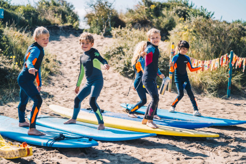 Kinderen in wetsuits oefenen met surfplanken op het zand bij Surfana Family Camp Bloemendaal, Glamping Noord-Holland.