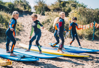 Niños con trajes de neopreno practicando con tablas de surf en la arena en Surfana Family Camp Bloemendaal, Glamping Noord-Holland.
