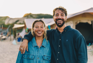 Two happy adults on the beach in front of their tent at Surfana Family Camp Bloemendaal Glamping Noord-Holland.