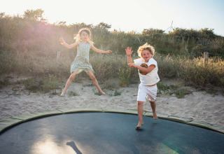 Dos niños saltan felices en una cama elástica en Surfana Family Camp Bloemendaal, Glamping Noord-Holland.
