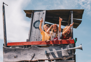 Tre børn leger i et træhus på Surfana Family Camp Bloemendaal, Glamping Noord-Holland under blå himmel.