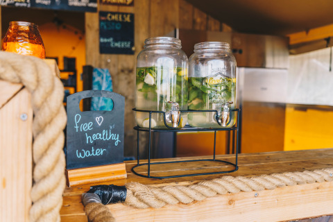 Agua saludable gratis con limón y hierbas en dispensadores de vidrio en Surfana Family Camp Bloemendaal glamping.