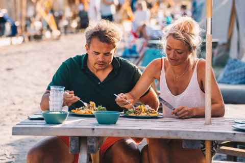 Una coppia si gode un pasto su un tavolo da picnic in spiaggia al Surfana Family Camp Bloemendaal.