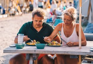Una pareja disfruta de una comida en una mesa de picnic en la playa en Surfana Family Camp Bloemendaal.