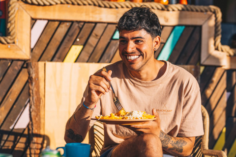 Ung mand smiler og spiser mad udendørs på Surfana Family Camp Bloemendaal - Glamping Noord-Holland.