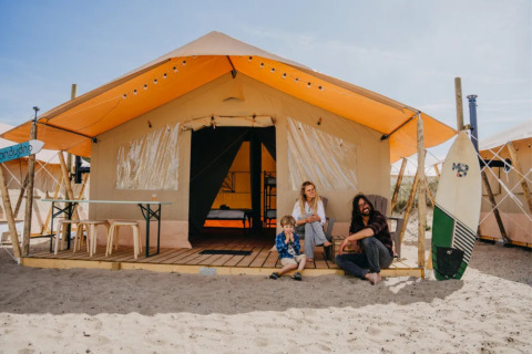 Famiglia seduta davanti a una tenda glamping al Surfana Family Camp Bloemendaal su una spiaggia di Noord-Holland.