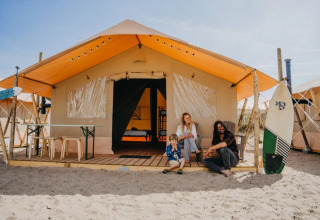 Gezin zit voor een glampingtent bij Surfana Family Camp Bloemendaal op het strand in Noord-Holland.