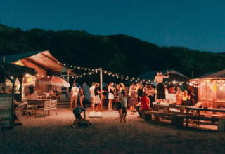 Avondsfeer bij Surfana Family Camp Bloemendaal met gezinnen, lichtjes en glamping tenten op het strand.