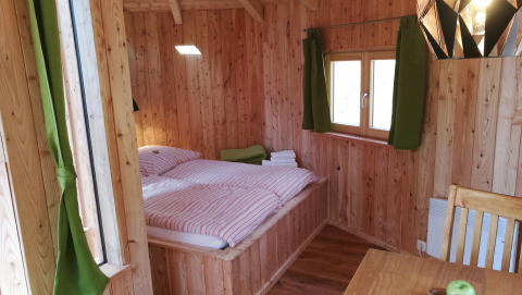 Cabane en bois avec lit double, rideaux verts et coin repas au Baumhaushotel Solling en Basse-Saxe, glamping.