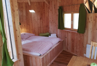 Agradable cabaña de madera con cama doble, cortinas verdes y comedor en Baumhaushotel Solling en Baja Sajonia.