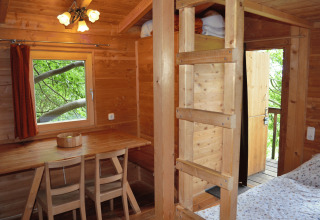 Innenansicht eines Baumhaushotels in Solling mit Holzmöbeln, Fenster und Leiter ins Hochbett.