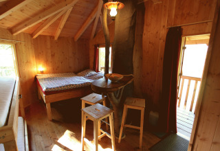 Interior view of a cozy treehouse with wooden walls, double bed, and stools at Baumhaushotel Solling glamping site.
