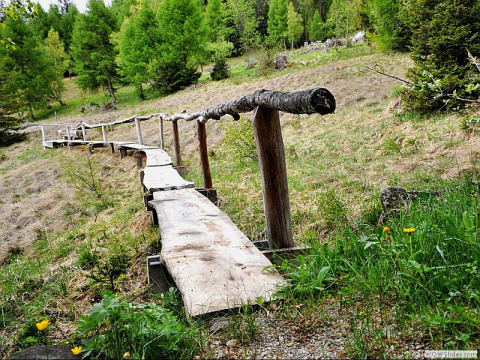 Passerella in legno con corrimano rustico tra l'erba al Glamping Sundelas - Zigeunerwagen Zwitserse Alpen.