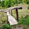 Wooden walkway with rustic railing winds through grass and trees at Glamping Sundelas - Zigeunerwagen Zwitserse Alpen.