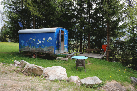 Glamping in carovana zingara nei pressi delle Alpi svizzere, decoro floreale, terrazza e bosco.
