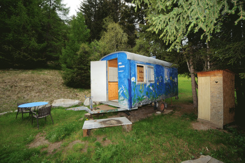 Glamping Sundelas - Zigeunerwagen Zwitserse Alpen, vrolijke woonwagen in bosrijk gebied met zitje en houten hutje.