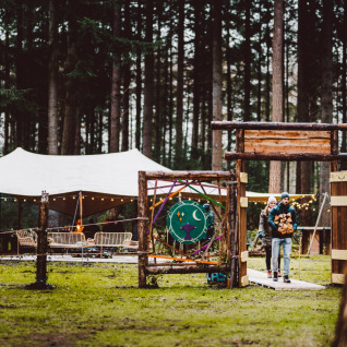 Koppel aan de ingang van glamping Winterwoods - Yurts Drenthe, met tenten en lichtjes in een bos.