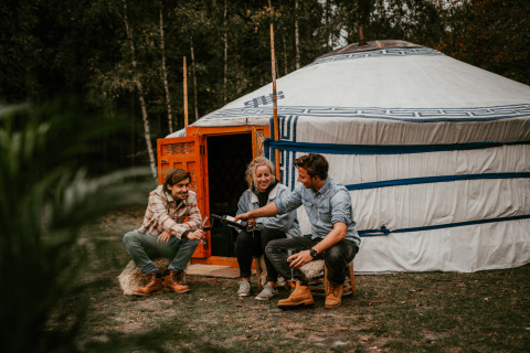 Drie mensen zitten buiten een yurt bij Winterwoods - Yurts Drenthe en genieten van glamping in de natuur.