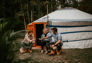 Drie mensen zitten buiten een yurt bij Winterwoods - Yurts Drenthe en genieten van glamping in de natuur.