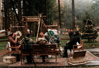 Groep ontspant rond kampvuur bij Winterwoods - Yurts Drenthe glamping, omgeven door winterbos.